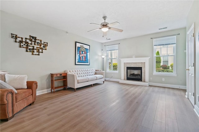 living area with visible vents, baseboards, light wood-type flooring, a tile fireplace, and a ceiling fan
