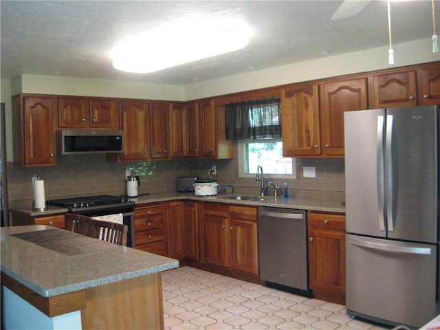 kitchen with brown cabinetry, a sink, appliances with stainless steel finishes, and backsplash