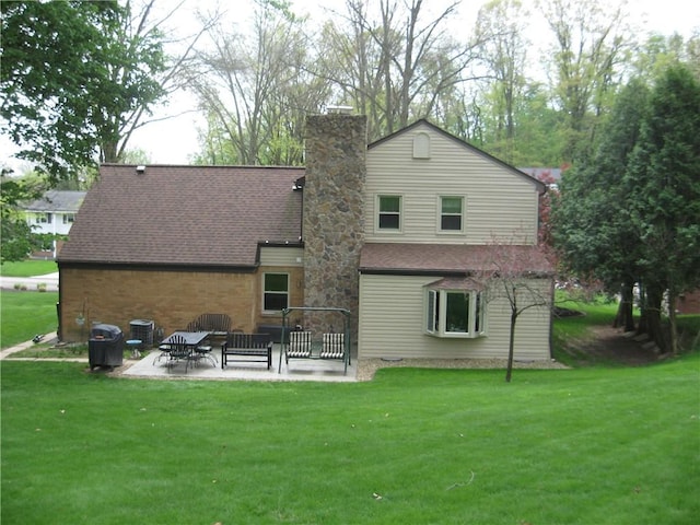 rear view of house with a patio, a shingled roof, a lawn, and a chimney