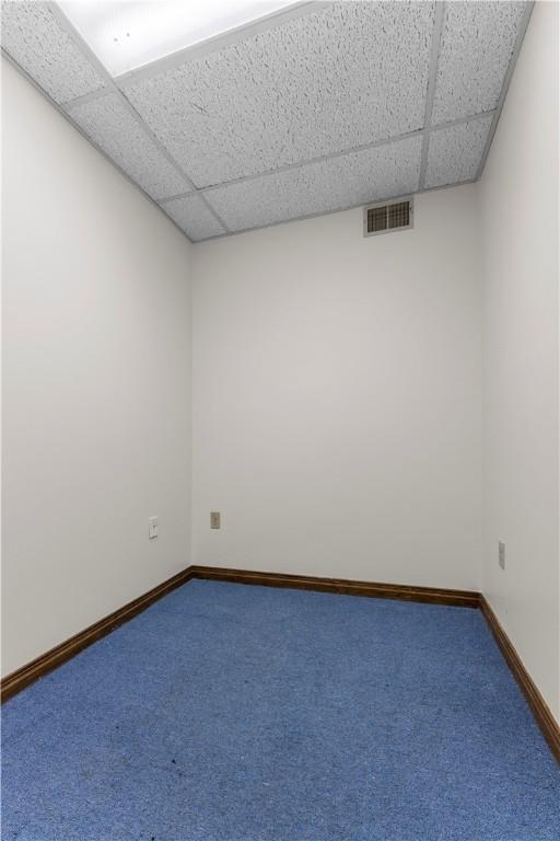carpeted empty room with baseboards, visible vents, and a paneled ceiling