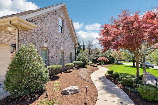 view of side of home with a yard, brick siding, and an attached garage