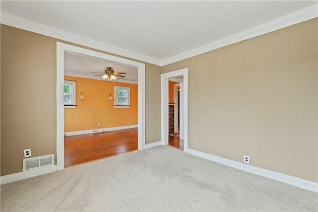 carpeted spare room with baseboards, ornamental molding, a ceiling fan, and visible vents