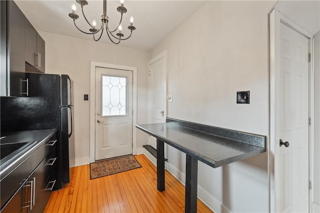 kitchen with dark countertops, light wood-type flooring, baseboards, black appliances, and an inviting chandelier