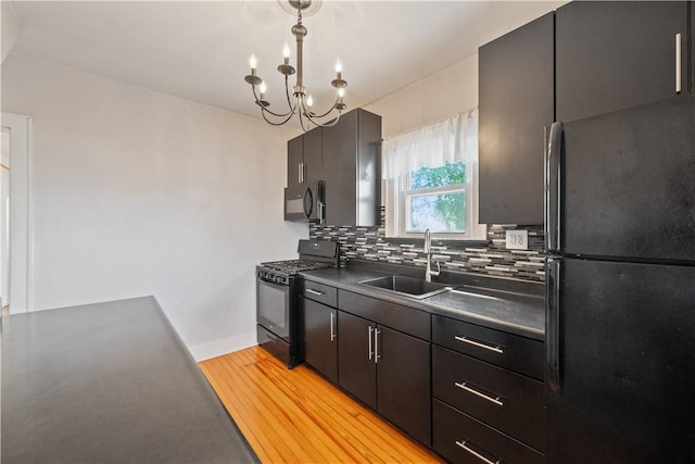 kitchen with decorative backsplash, dark countertops, a sink, light wood finished floors, and black appliances
