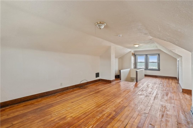additional living space with a textured ceiling, visible vents, vaulted ceiling, light wood-type flooring, and baseboards