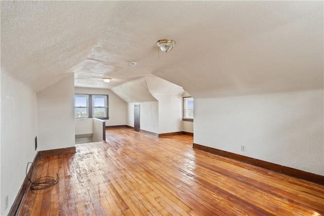 additional living space with light wood-style floors, baseboards, vaulted ceiling, and a textured ceiling