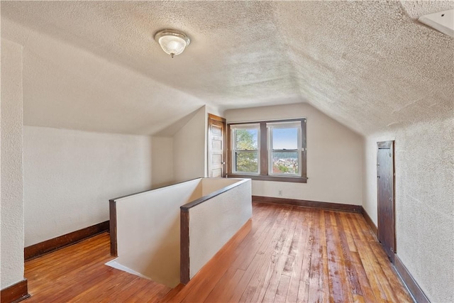 additional living space featuring wood-type flooring, baseboards, a textured ceiling, and lofted ceiling