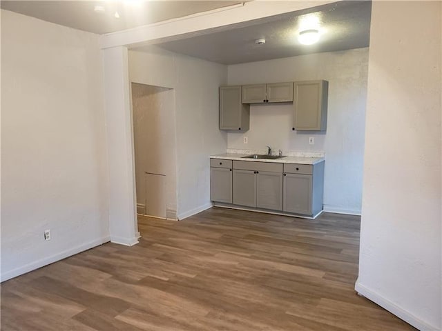 kitchen with baseboards, a sink, dark wood-type flooring, and gray cabinetry