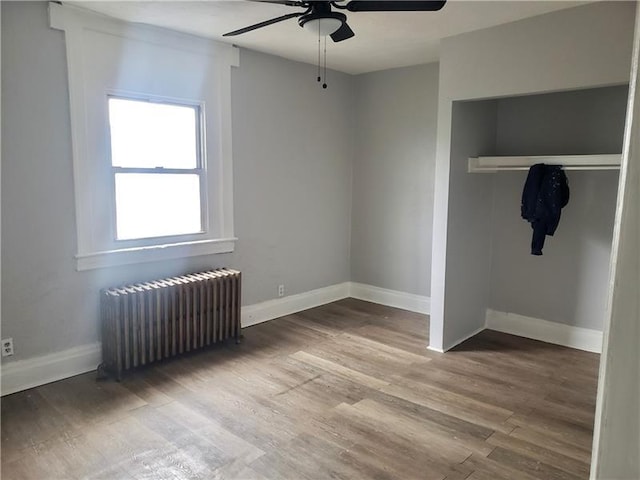 unfurnished bedroom with a closet, radiator, wood finished floors, baseboards, and ceiling fan