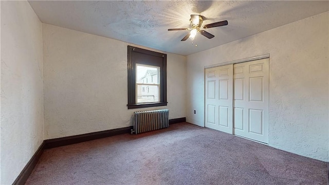 unfurnished bedroom featuring a textured wall, carpet floors, radiator heating unit, a ceiling fan, and a closet