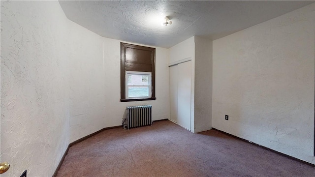 carpeted spare room with baseboards, radiator, and a textured wall