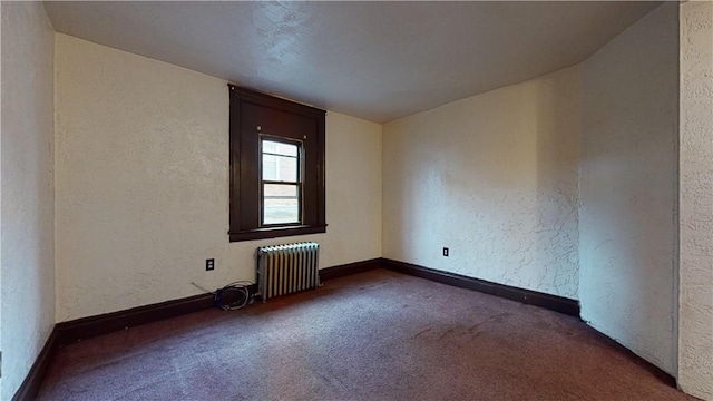 empty room featuring radiator, a textured wall, baseboards, and carpet flooring