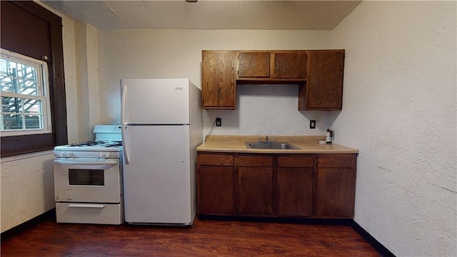 kitchen featuring a sink, white appliances, light countertops, baseboards, and dark wood-style floors