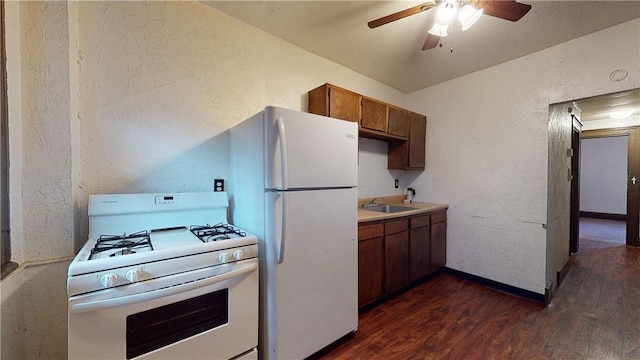 kitchen featuring a textured wall, white appliances, ceiling fan, a sink, and dark wood finished floors