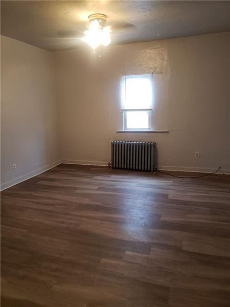 spare room with baseboards, dark wood finished floors, and radiator heating unit