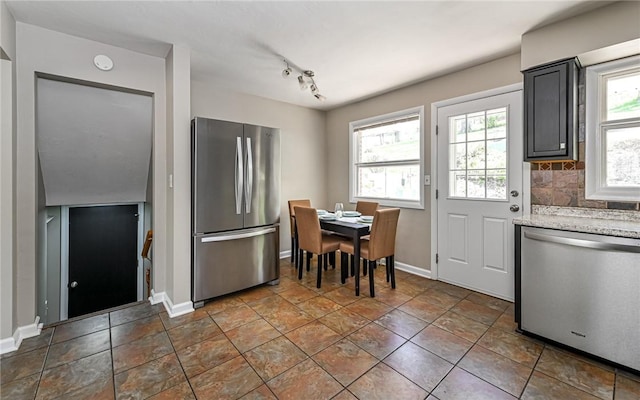 kitchen with baseboards, appliances with stainless steel finishes, light stone counters, and tasteful backsplash