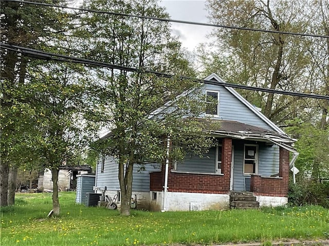 bungalow-style home featuring brick siding, central AC unit, and a front lawn