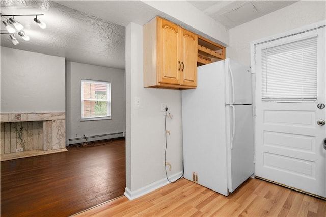 kitchen featuring freestanding refrigerator, light brown cabinetry, light wood-style floors, baseboard heating, and a textured ceiling