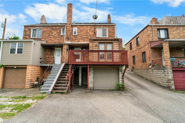 back of property featuring an attached garage, a chimney, driveway, and stairway