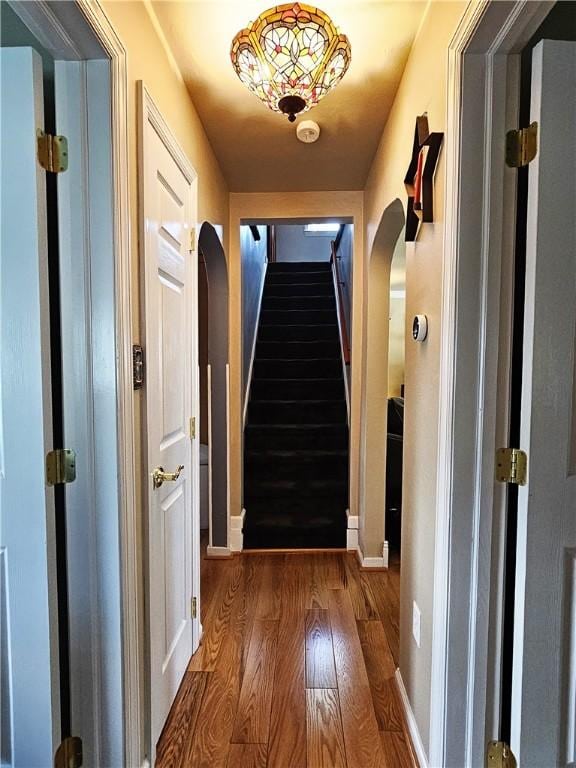 corridor with stairway, arched walkways, baseboards, and wood finished floors