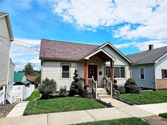 view of front of property with fence, roof with shingles, and a front lawn