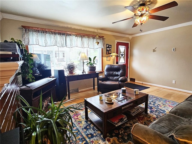 living room featuring a ceiling fan, visible vents, wood finished floors, baseboards, and ornamental molding