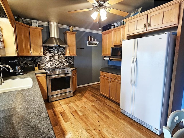 kitchen with wall chimney range hood, a sink, stainless steel gas range oven, freestanding refrigerator, and a ceiling fan