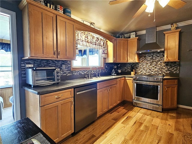 kitchen with wall chimney range hood, backsplash, a ceiling fan, appliances with stainless steel finishes, and a sink