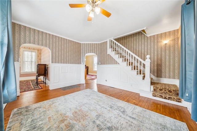interior space featuring ceiling fan, crown molding, arched walkways, wood-type flooring, and wallpapered walls
