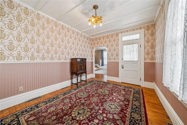 entrance foyer featuring crown molding, arched walkways, wainscoting, and hardwood / wood-style flooring