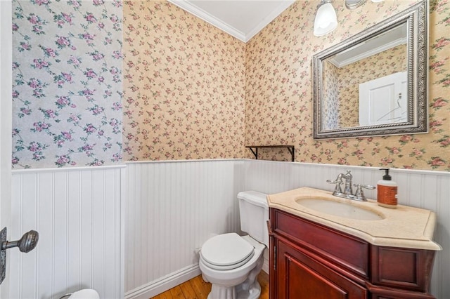 half bath featuring crown molding, vanity, wood finished floors, toilet, and a wainscoted wall