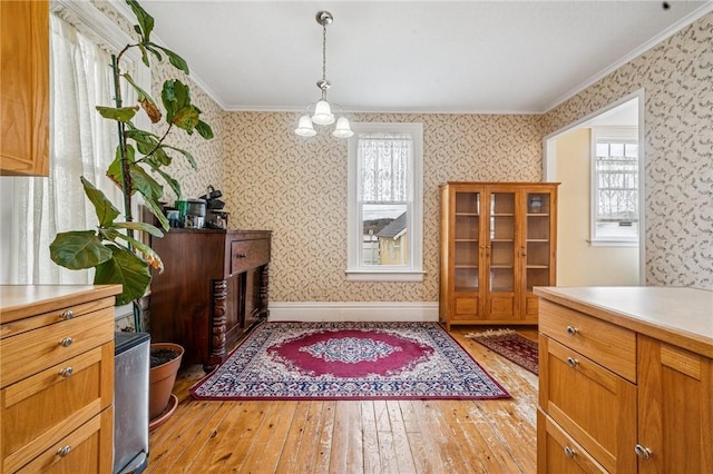 dining room with light wood-type flooring, ornamental molding, baseboards, and wallpapered walls