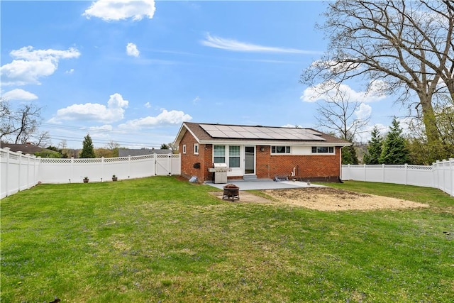 rear view of house featuring solar panels, brick siding, a fenced backyard, an outdoor fire pit, and a patio