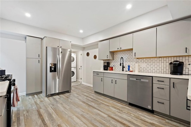 kitchen featuring stacked washer and dryer, light countertops, gray cabinets, a sink, and stainless steel appliances