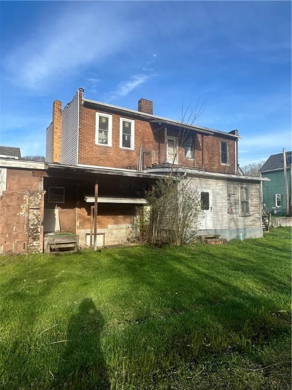 back of property with brick siding, a lawn, and a chimney