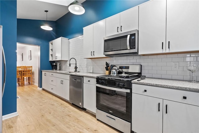 kitchen with light wood-type flooring, white cabinets, a sink, backsplash, and stainless steel appliances