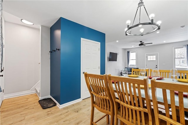 dining area featuring light wood-type flooring, plenty of natural light, ceiling fan with notable chandelier, and baseboards