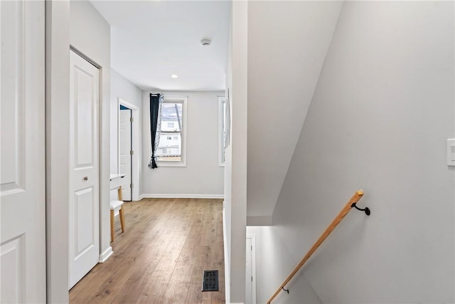 corridor with baseboards, an upstairs landing, light wood-style flooring, and visible vents