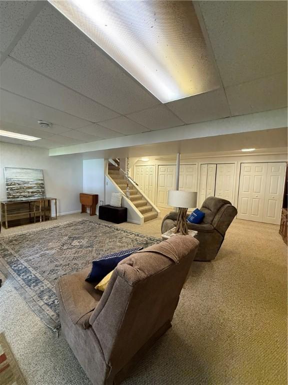 carpeted living room featuring a drop ceiling and stairway