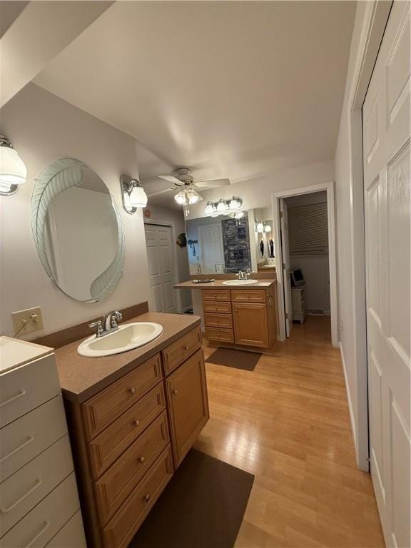 bathroom featuring a sink, a ceiling fan, wood finished floors, and two vanities