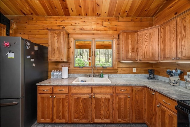 kitchen featuring freestanding refrigerator, wooden walls, wooden ceiling, and a sink