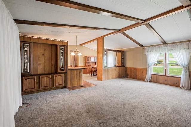 unfurnished living room featuring wooden walls, a wainscoted wall, lofted ceiling with beams, and light colored carpet