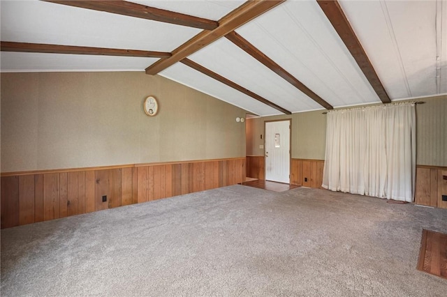 carpeted spare room with wooden walls, wainscoting, and vaulted ceiling with beams