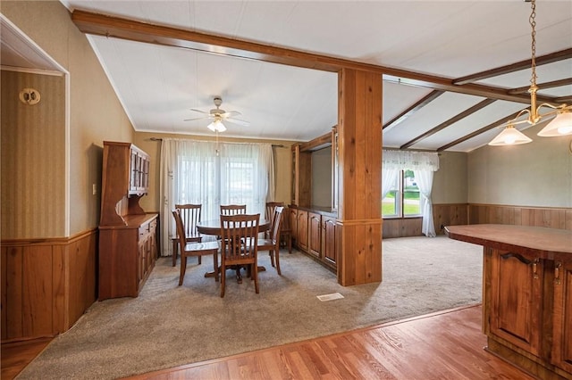 dining room with a ceiling fan, wainscoting, wood walls, wood finished floors, and vaulted ceiling with beams