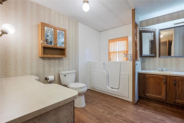 bathroom with vanity, wood finished floors, a washtub, toilet, and wallpapered walls
