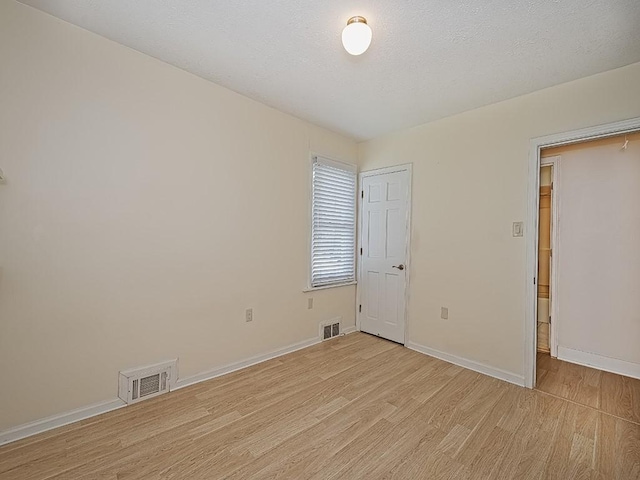 unfurnished room with baseboards, a textured ceiling, light wood-style flooring, and visible vents