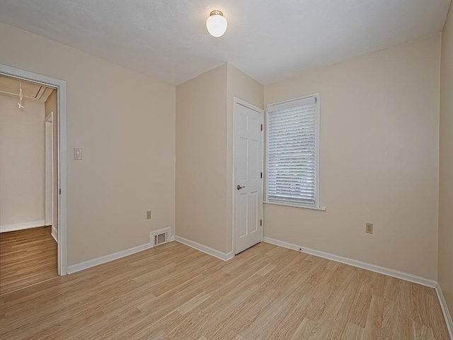 unfurnished room featuring baseboards, attic access, light wood-style flooring, and visible vents