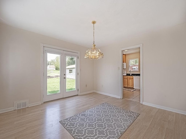 unfurnished dining area featuring visible vents, an inviting chandelier, baseboards, light wood-type flooring, and french doors