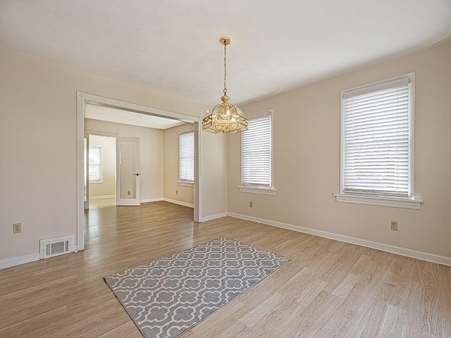 unfurnished dining area with baseboards, a notable chandelier, light wood-type flooring, and visible vents