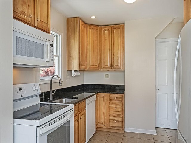 kitchen featuring a sink, dark stone countertops, light tile patterned flooring, and white appliances
